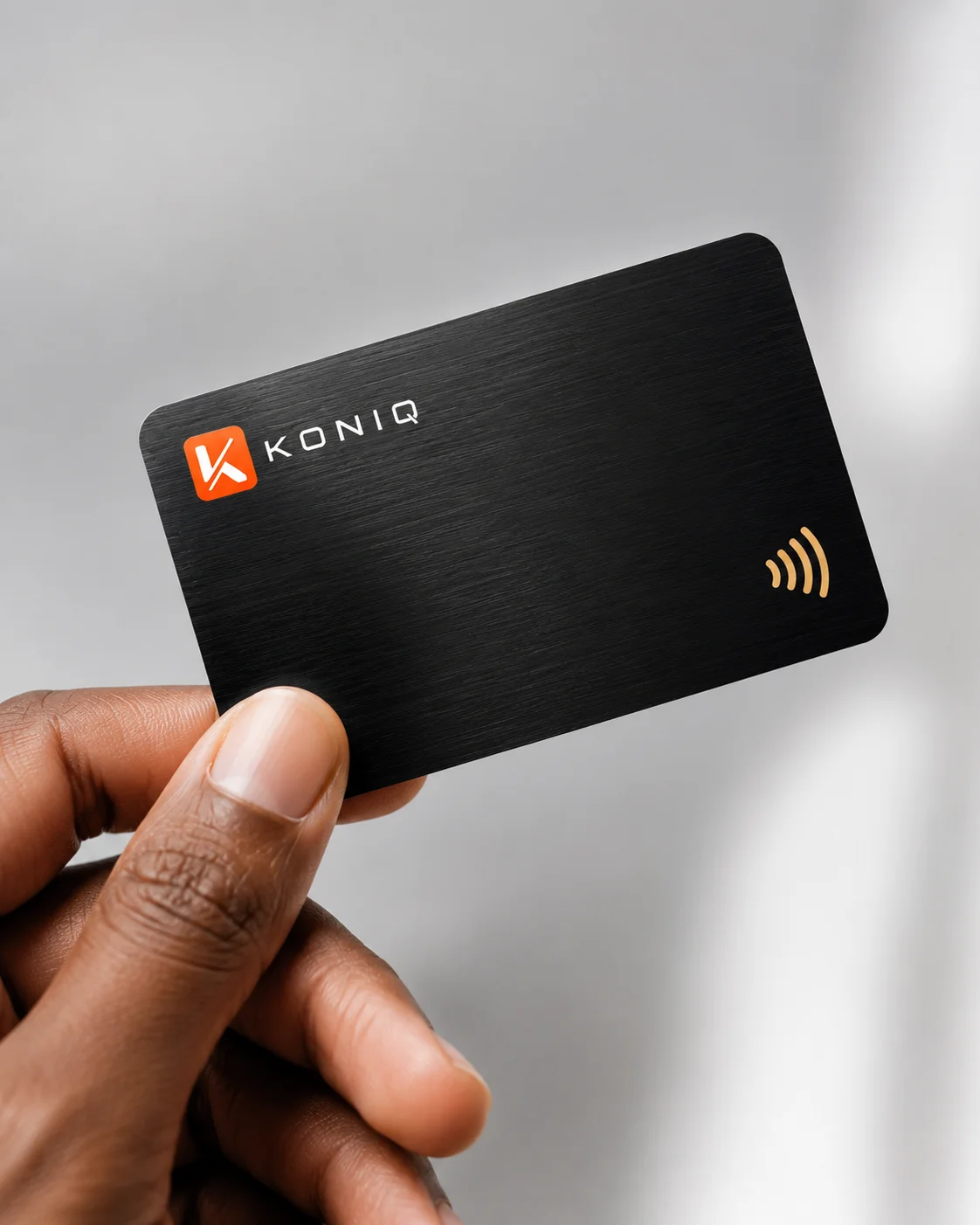 Carte Koniq noire brossée tenue en main, signature orange et puce NFC